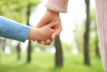 Eine kleinere Hand hält eine größere Hand im Freien