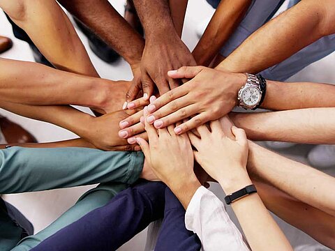 Hände mehrerer Personen liegen übereinander als Symbol für gemeinsames Arbeiten im Team